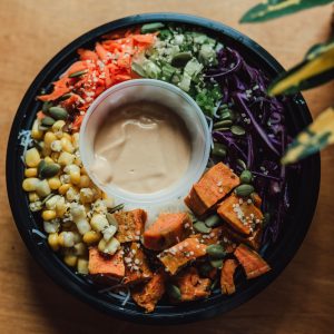 A healthy vegan Buddha Bowl made by Green Heart Kitchen Kingsville with carrots, greens, cabbage, sweet potato, corn and dressing.