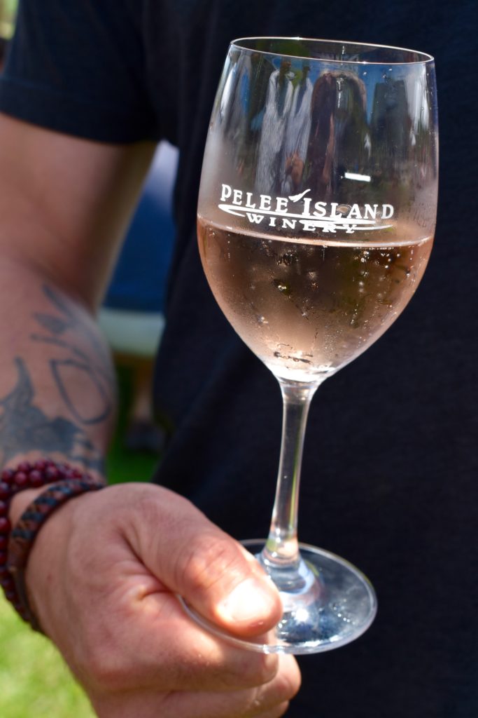A man with a tattooed arm holding a glass of Pelee Island Winery Lola Sparkling Rosé Blush VQA Ontario rosé wine at the Pelee Island Winery Pavilion on Pelee Island.