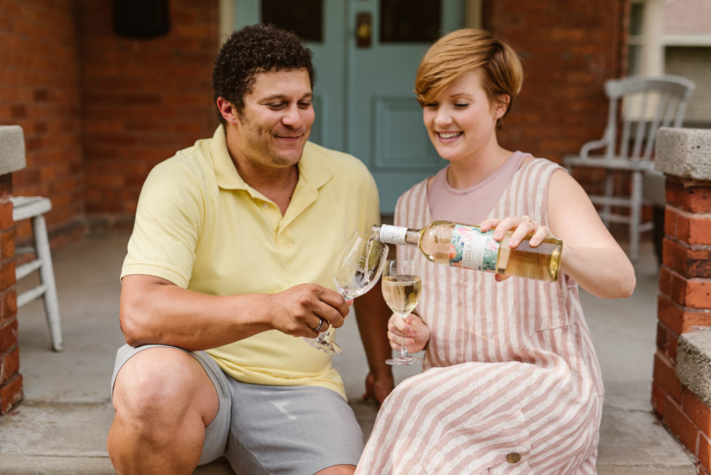 Two people sitting on front porch in Kingsville, Ontario pouring a bottle of Pelee Island Winery Lola Pinot Grigio VQA Ontario into two Pelee Island Winery glasses in the summer. 